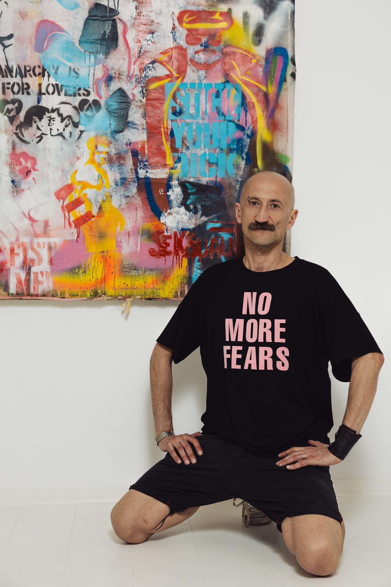 Mężczyzna w czarnej koszulce z napisem 'NO MORE FEARS', przed kolorowym graffiti, styl uliczny, moda z kulturą