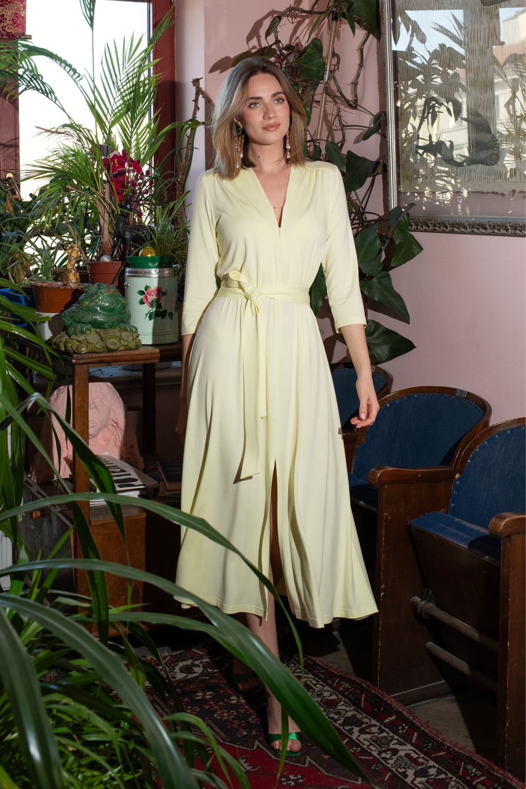 Kobieta w żółtej sukience midi z wiązanym pasem, w stylu self-care fashion, wśród roślin i vintage mebli