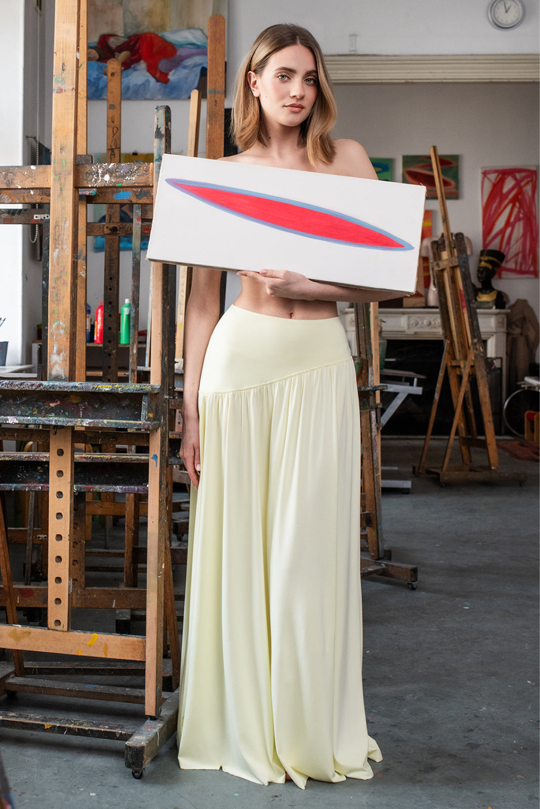 Kobieta w żółtej sukience trzyma obraz w artystycznym atelier