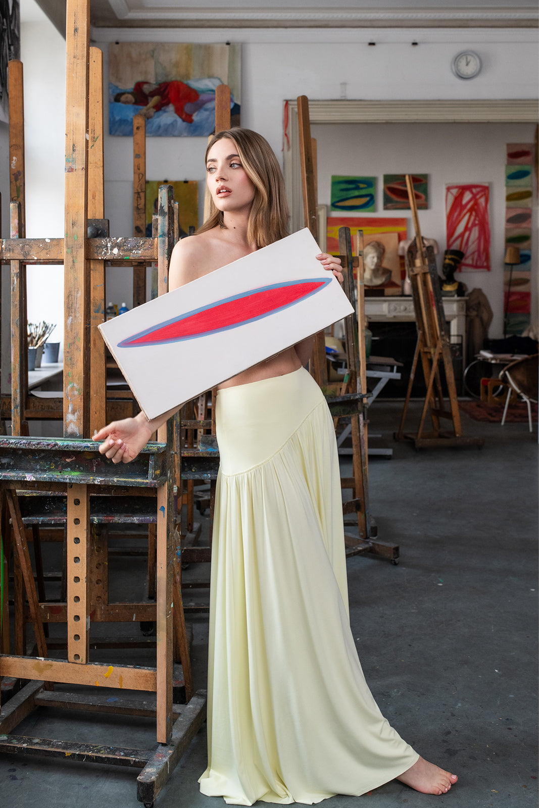 Kobieta w żółtej sukience trzyma obraz w artystycznym atelier, stylowy i wygodny strój