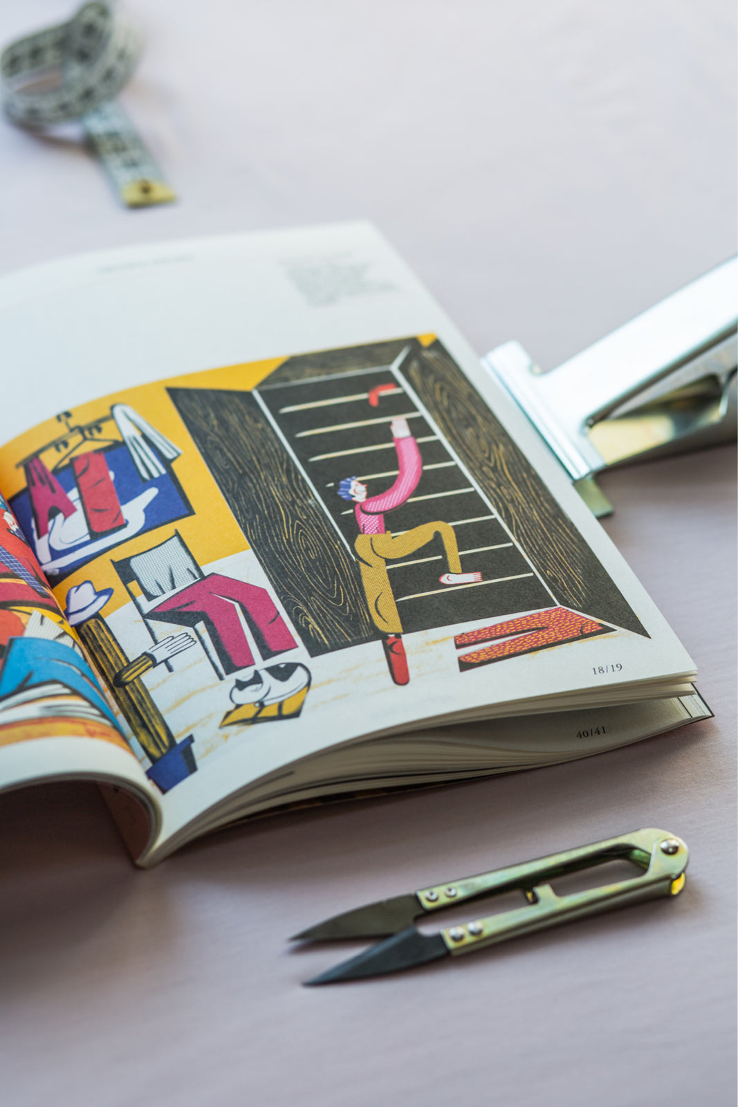 Książka z ilustracjami artystycznymi, miarka i nożyczki do szycia – inspiracja dla projektantów odzieży i miłośników mody.