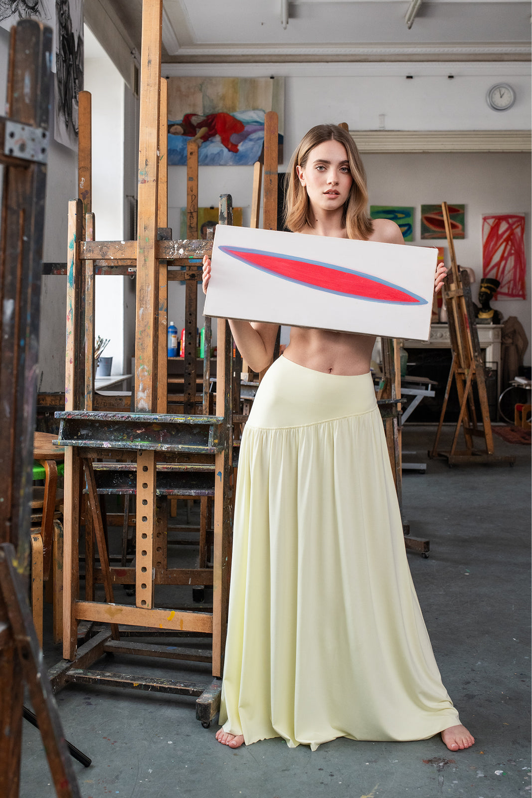 Kobieta w żółtej sukience trzyma obraz w artystycznym atelier