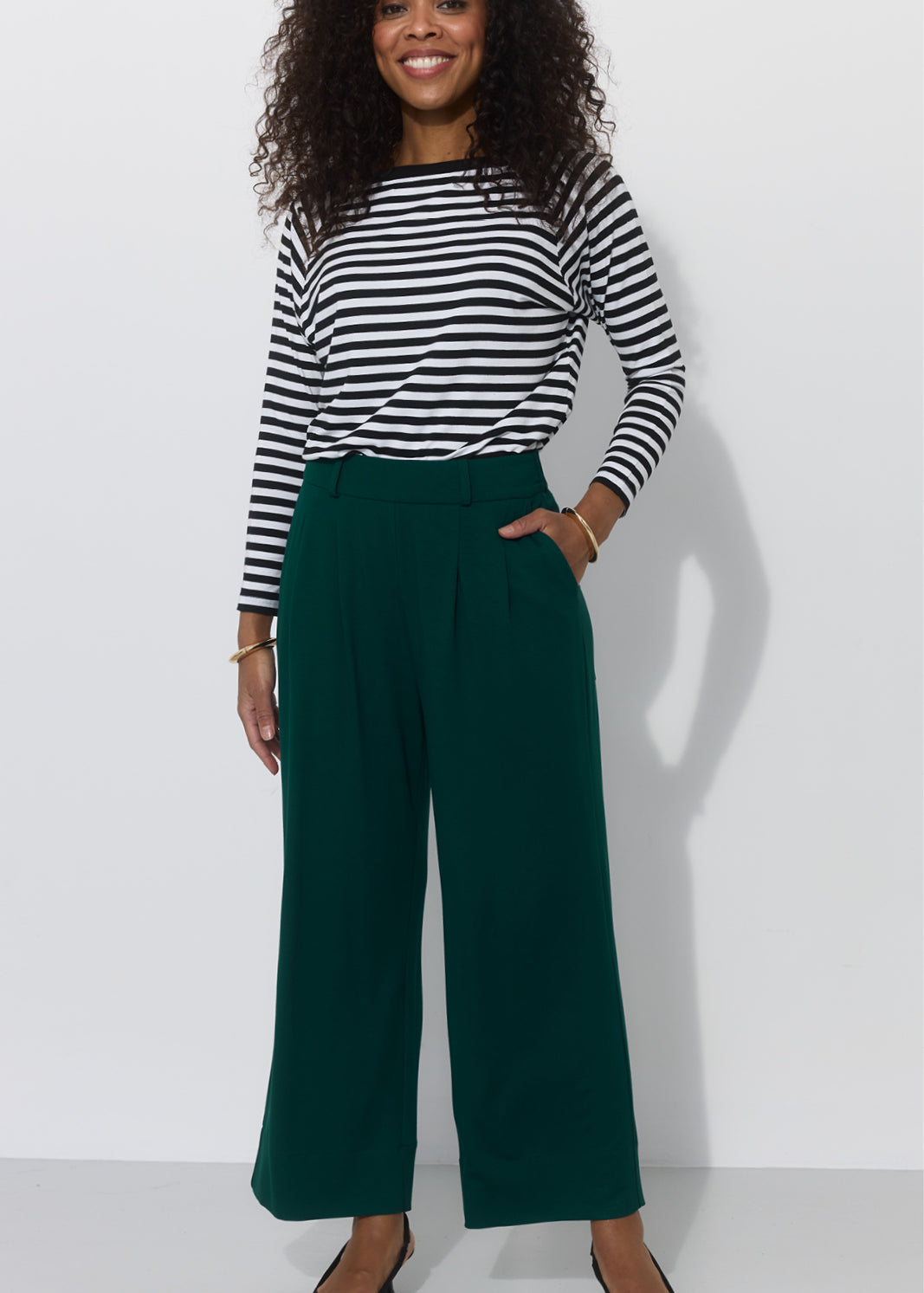 Kobieta w zielonych spodniach typu culottes i koszulce w paski, stylowy strój na co dzień