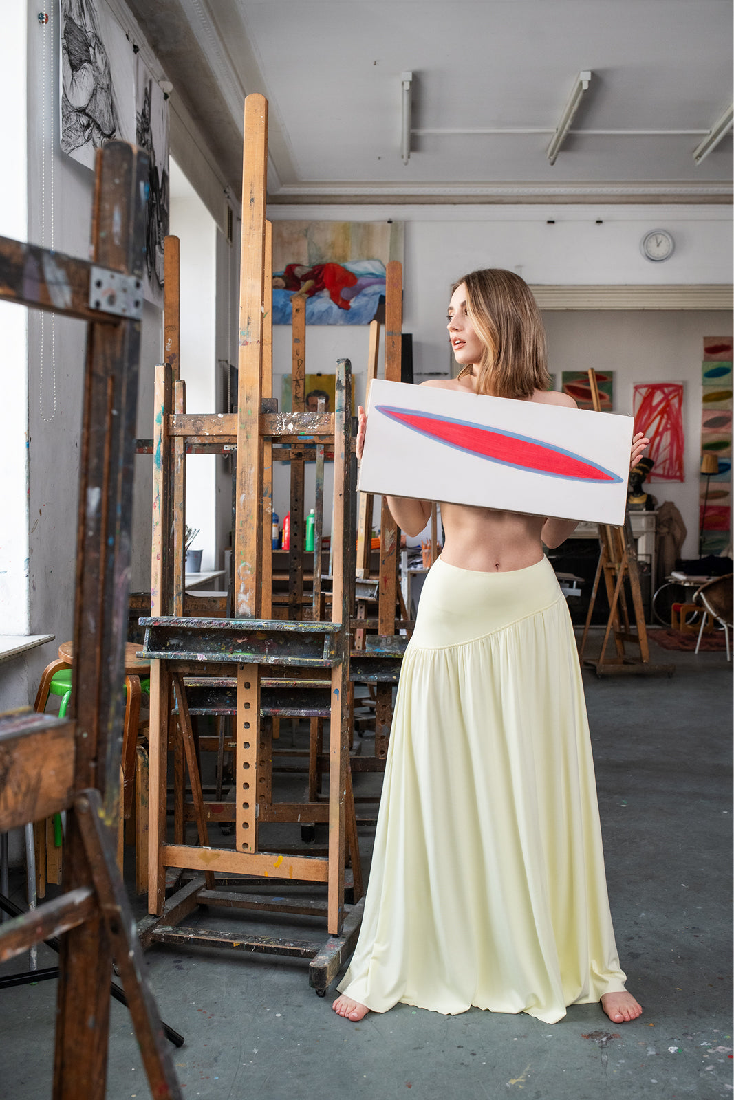 Kobieta w żółtej sukience trzyma obraz w artystycznym atelier, stylowy i wygodny strój