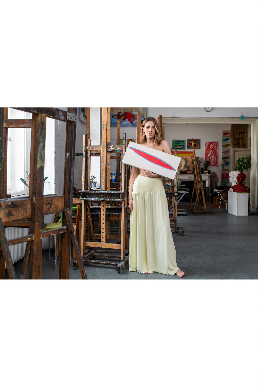 Kobieta w żółtej sukience trzyma obraz w artystycznym atelier, stylowy i wygodny strój