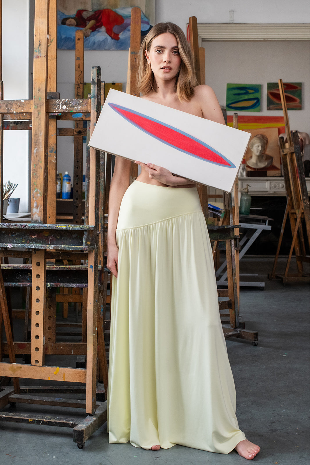 Kobieta w żółtej sukience trzyma obraz w artystycznym atelier
