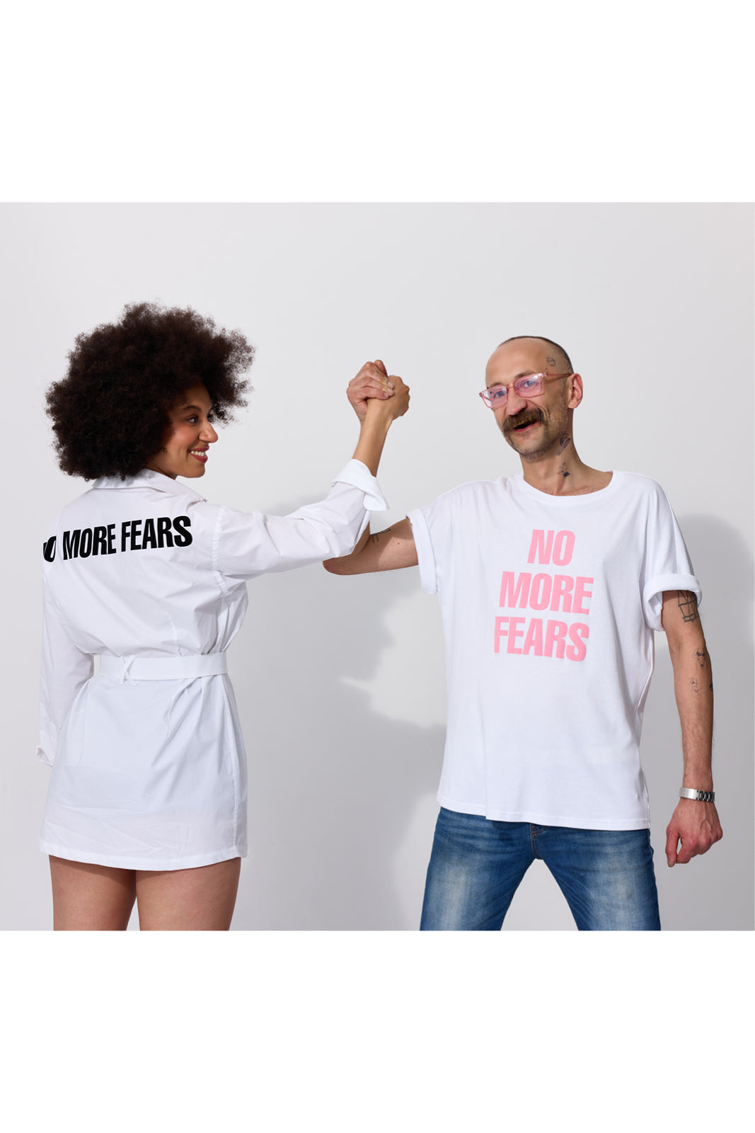Kobieta w białej sukience i mężczyzna w koszulce z napisem NO MORE FEARS, trzymający się za ręce