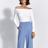 Kobieta w białej bluzce z odkrytymi ramionami i niebieskich spodniach wide leg, stylowa i wygodna moda