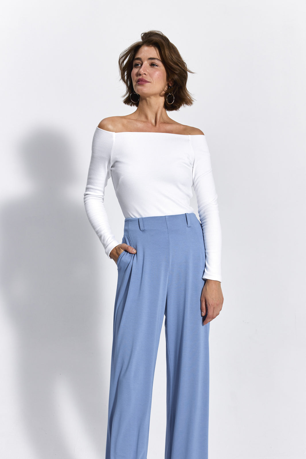 Kobieta w białej bluzce z odkrytymi ramionami i niebieskich spodniach wide leg, stylowa i wygodna moda